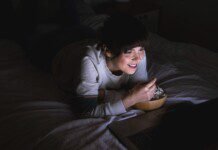 Jovem mulher assistindo a um filme no laptop na cama. Aconchegante, estilo de vida, em casa, relaxar, relaxar, lazer, uma pessoa, noite, usando tecnologia, usando laptop, assistindo tv, netflix, streaming, sorriso, sorrindo.