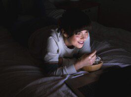 Jovem mulher assistindo a um filme no laptop na cama. Aconchegante, estilo de vida, em casa, relaxar, relaxar, lazer, uma pessoa, noite, usando tecnologia, usando laptop, assistindo tv, netflix, streaming, sorriso, sorrindo.