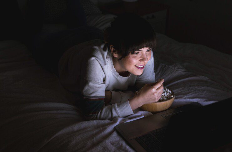Jovem mulher assistindo a um filme no laptop na cama. Aconchegante, estilo de vida, em casa, relaxar, relaxar, lazer, uma pessoa, noite, usando tecnologia, usando laptop, assistindo tv, netflix, streaming, sorriso, sorrindo.